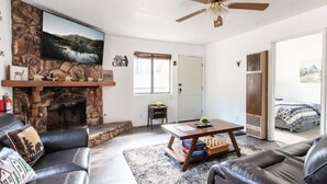 Una sala de estar con chimenea de piedra, sofás de cuero, una mesa de centro y un ventilador de techo.