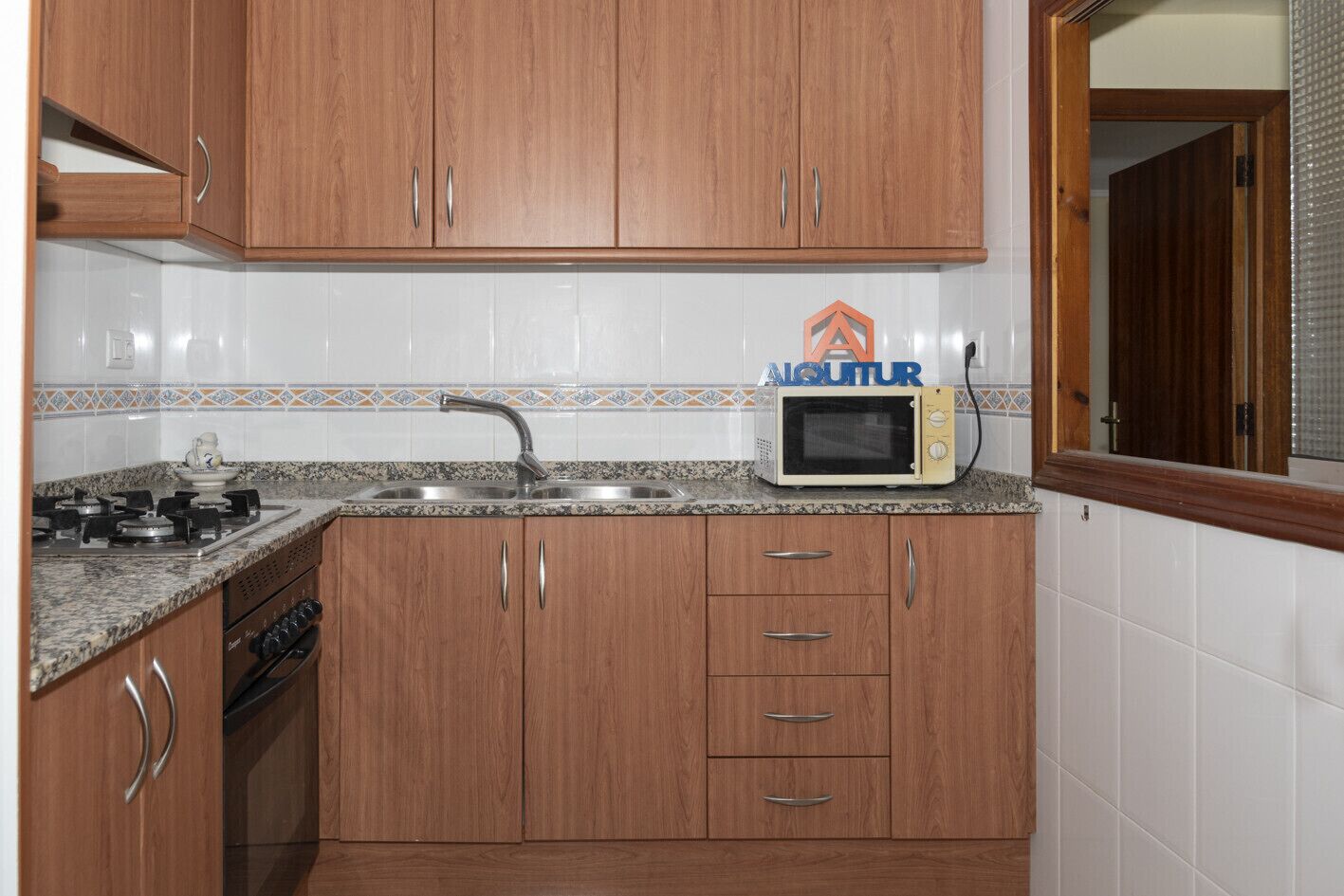 A kitchen with wooden cabinets, a granite countertop, a microwave, a sink, and a stove.