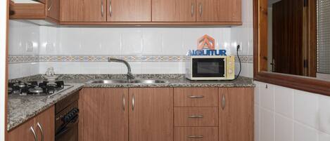 A kitchen with wooden cabinets, a granite countertop, a microwave, a sink, and a stove.