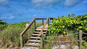 Un escalier en bois menant à un niveau supérieur, entouré d’une végétation luxuriante et sous un ciel dégagé.