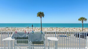 Une vue sur la plage avec une balustrade blanche, deux chaises et une table recouverte d’une nappe.