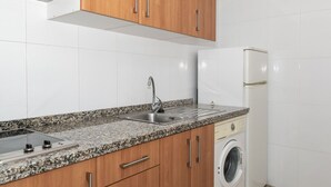 Una cocina con encimera de granito, pileta de acero inoxidable, armarios de madera y lavadora integrada.