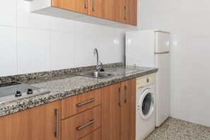 A kitchen with a granite countertop, stainless steel sink, wooden cabinets, and a built-in washing machine. - MIRALMAR, 10º-69 (Cullera)