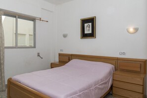 A bedroom with a single bed, a bedside table, a nightstand, a framed picture on the wall, and a wall-mounted light fixture. - MIRALMAR, 10º-69 (Cullera)