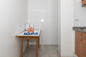 A small kitchen with white tiles, a wooden table with a logo, and a granite countertop. - MIRALMAR, 10º-69 (Cullera)
