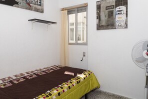 A small, single-bed room with a window, a wall-mounted shelf, and a wall-mounted fan. - MIRALMAR, 10º-69 (Cullera)