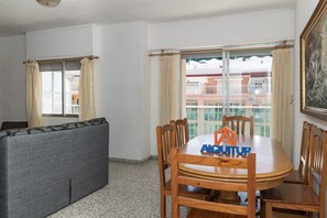 A dining area with a round wooden table, six chairs, and a sofa. A logo with "ALQUITOR" is on the table. - MIRALMAR, 10º-69 (Cullera)