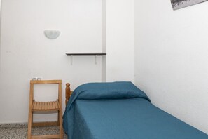 A small, single-bed room with a wooden chair, a wall-mounted shelf, and a light fixture. - MIRALMAR, 10º-69 (Cullera)