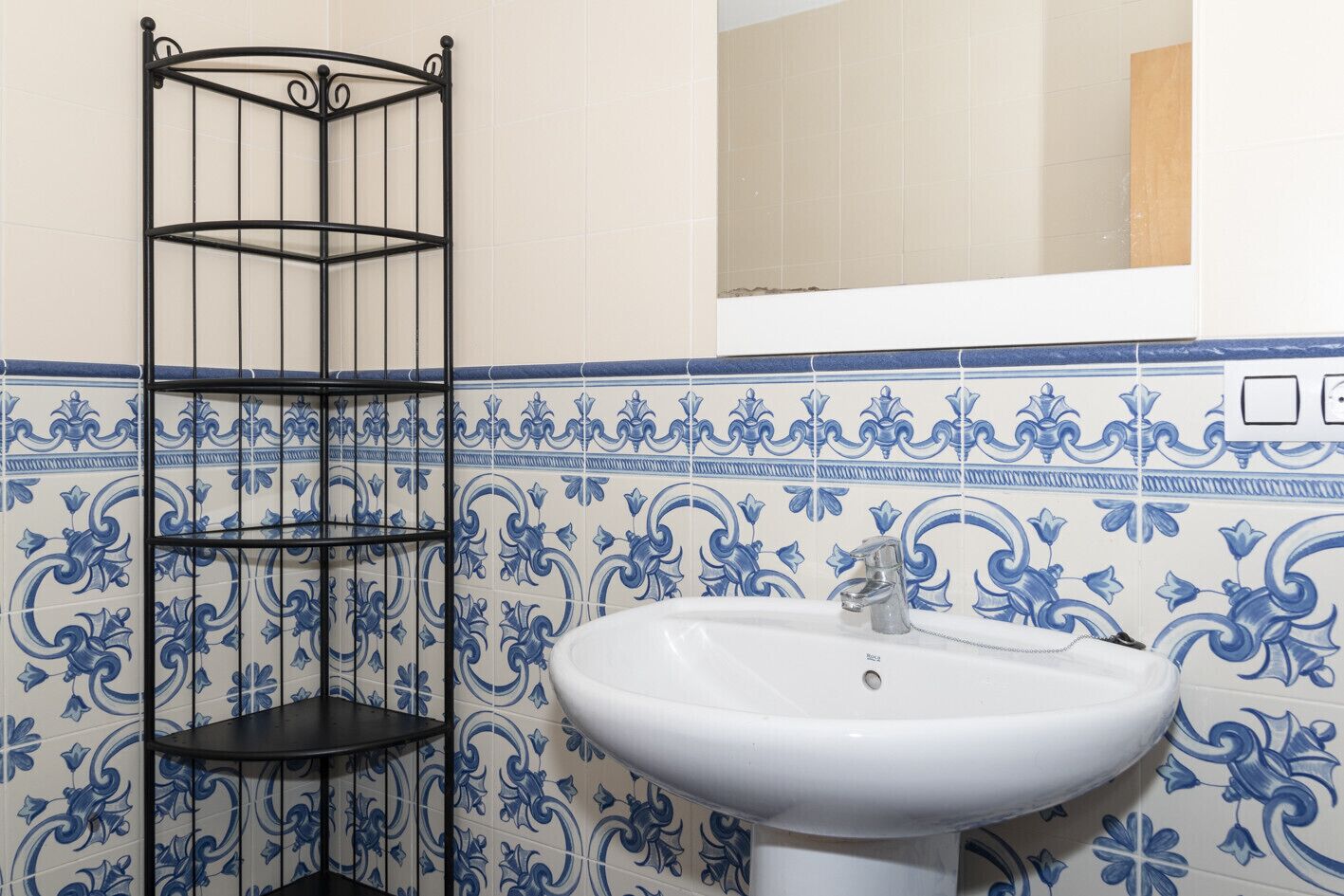 A bathroom with a white sink, a black metal shelf unit, and blue and white patterned tiles.