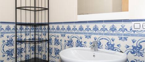 A bathroom with a white sink, a black metal shelf unit, and blue and white patterned tiles.