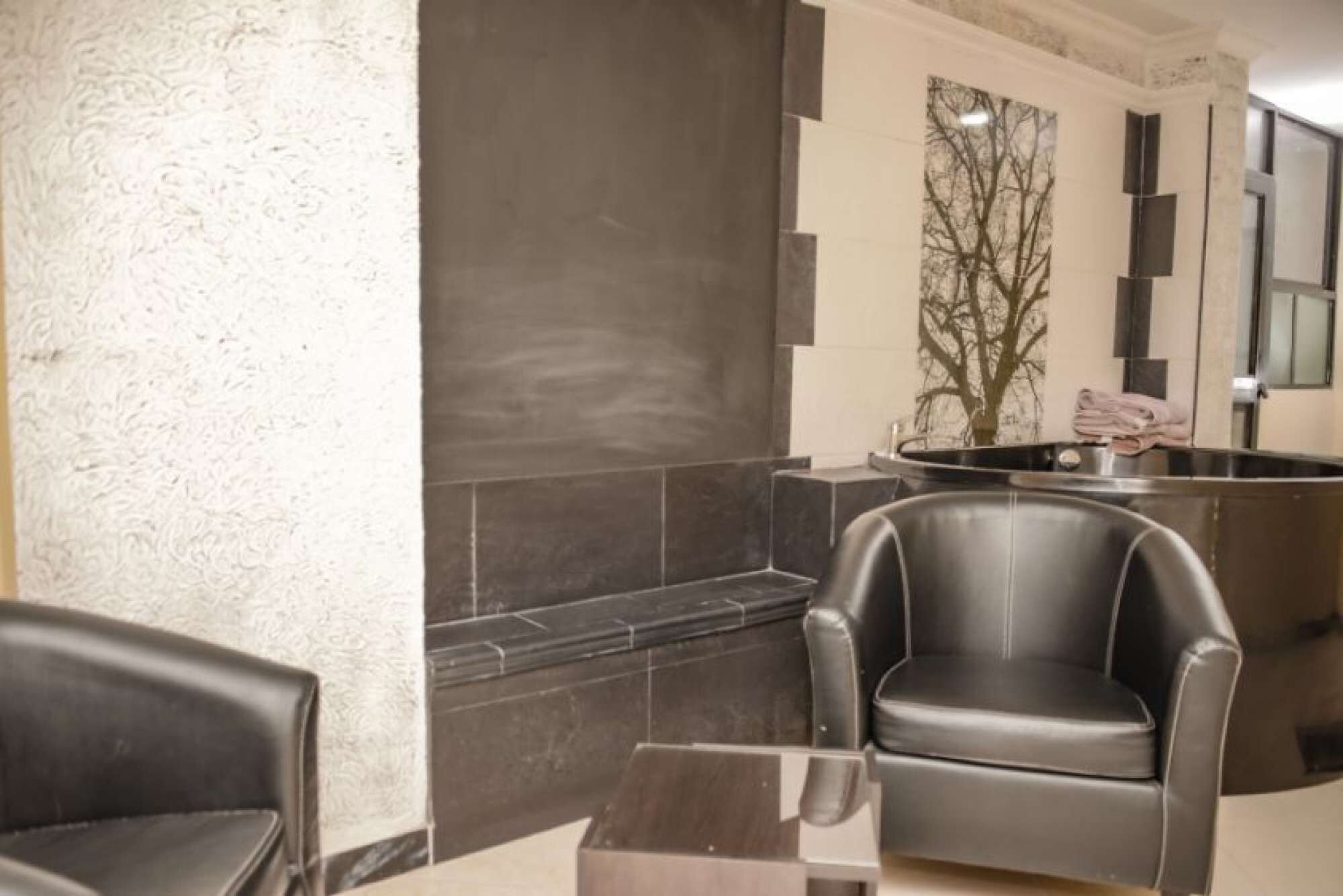 Une salle de bain moderne avec une grande baignoire, un coin salon avec deux fauteuils et un miroir.