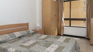 Een slaapkamer met een bed, een houten garderobe, een nachtkastje met een lamp en een raam met gordijnen.