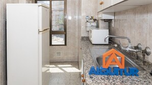 Een keuken met een koelkast, een raam, een spoelbak en een boiler.