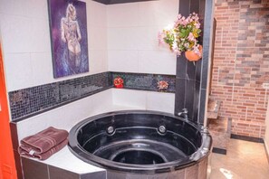 Ein Wellnessraum mit einer schwarzen Whirlwanne, einem Handtuch, einer Wand mit Mosaikfliesen und einer Backsteinwand.