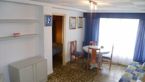Habitació petita i funcional amb llit, taula, cadires, moble i finestra amb cortines.