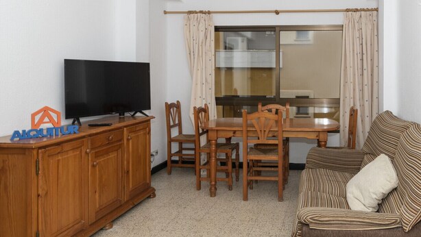 A living room with a TV on a wooden cabinet, a dining table with chairs, and a striped sofa. - ESTIRPE, 2º-4 (Cullera)