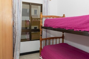 Uma cama beliche com estrutura de madeira e roupa de cama rosa, uma janela com cortinas e uma porta de madeira.