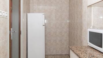 Een kleine kitchenette met een witte koelkast, een magnetron en een granieten aanrecht.