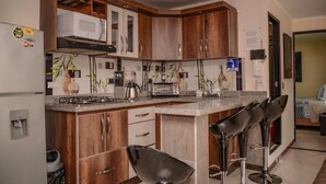 A kitchen with wooden cabinets, a microwave, a stove, a toaster, and a coffee maker. There are three bar stools and a sign indicating a water fountain. - 2 Bedroom Hot tub security AC Lleras area (medellin)