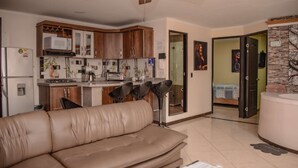 A modern kitchen with wooden cabinets, a built-in microwave, and a gas stove. There is a beige leather sofa in the living area and a dining table with chairs. The room has a ceiling fan and a stone accent wall. - 2 Bedroom Hot tub security AC Lleras area (medellin)