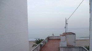 En takterrass med ett golv täckt av röda tegelpannor, en vit vägg och utsikt över stranden och havet.