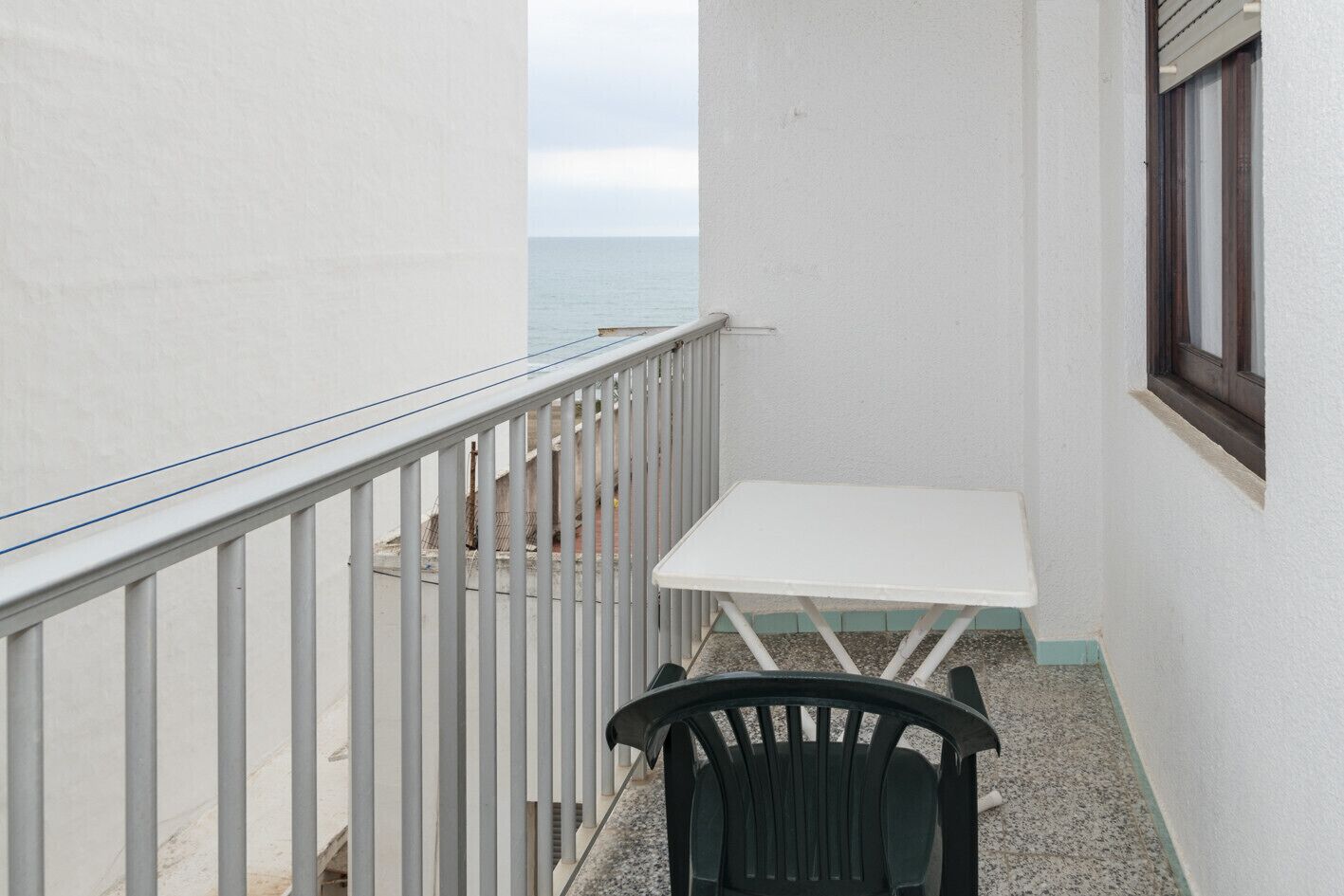 A balcony with a white table and a black chair, overlooking a body of water.