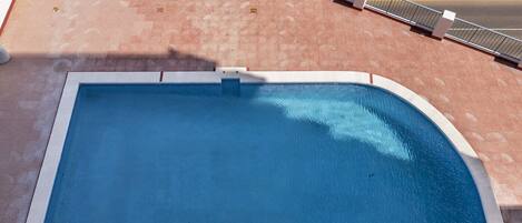 A rectangular swimming pool with a white border, surrounded by a red-tiled deck and a metal railing.