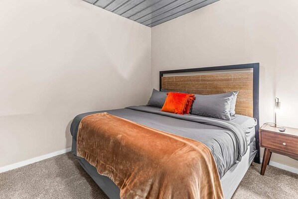 Un lit bien fait, avec une tête de lit en bois, une literie grise et un plaid marron.