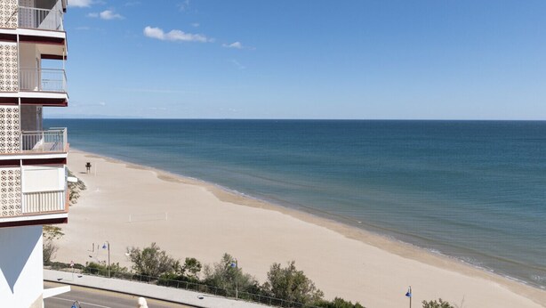 Um hotel à beira-mar com uma praia de areia, céu azul límpido e mar calmo.