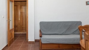 Um quarto com porta de madeira, um sofá cinzento e uma cadeira de madeira.