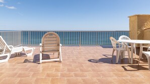 Terraço com vista para o mar, com cadeiras e mesa de plástico branco.