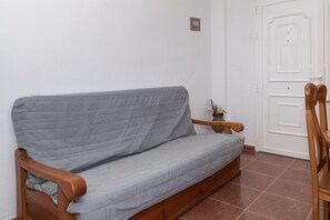 A grey sofa with wooden armrests and legs, positioned against a white wall with a door and a small picture frame. - PLENO SOL, 45 (Faro de Cullera)
