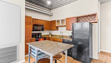A compact kitchen with wooden cabinets, a black refrigerator, a microwave, and a granite countertop.