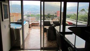 A view from a balcony with a pool, outdoor seating, and a cityscape in the background.
