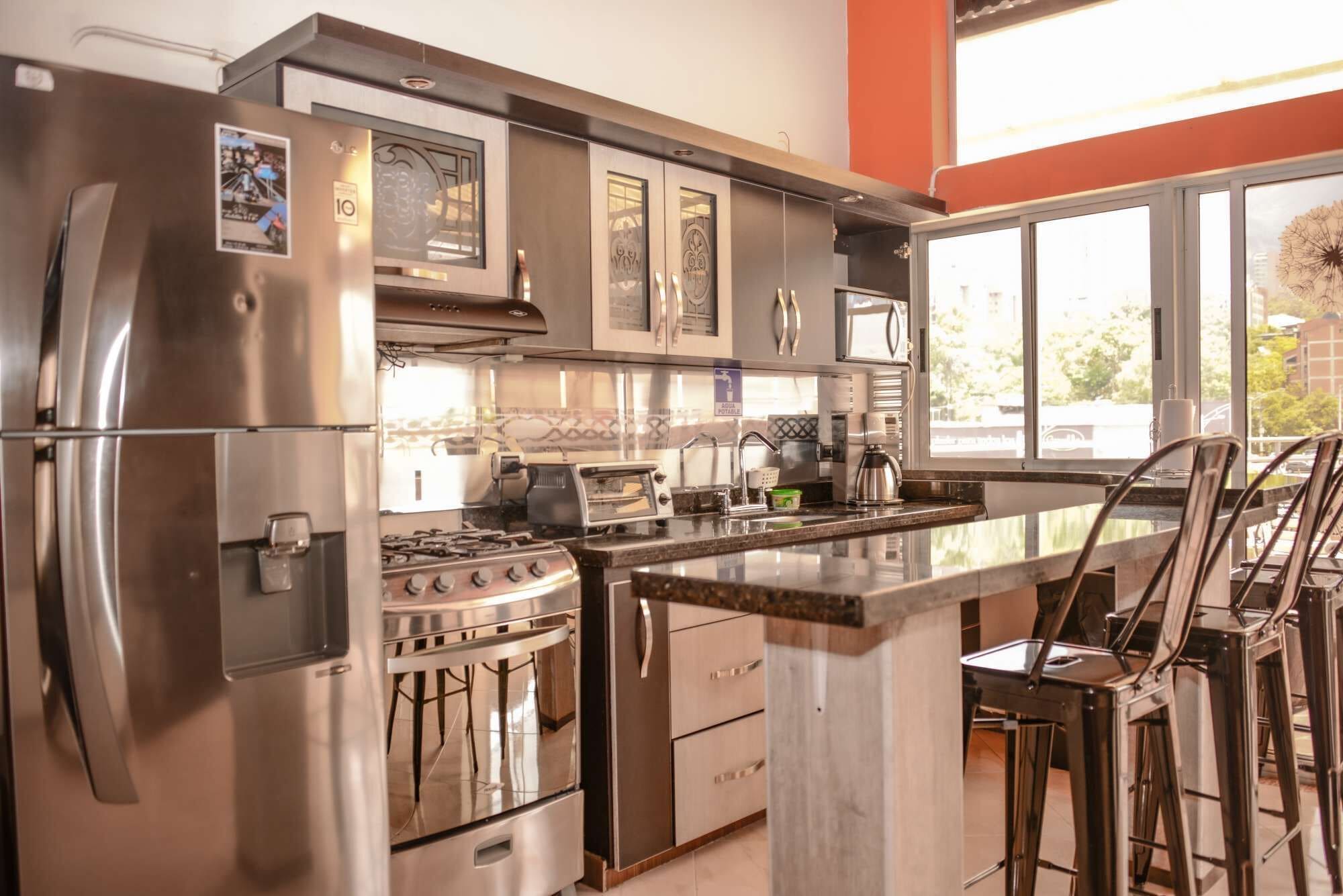 Une cuisine moderne équipée d’appareils électroménagers en acier inoxydable, d’une cuisinière à gaz et d’un coin bar avec des tabourets.