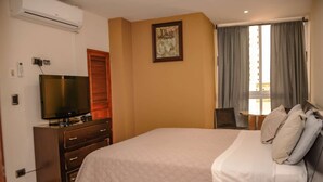 A hotel room with a bed, a TV, a desk, and a window with curtains.
