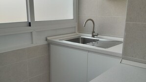 Una cocina con un lavamanos de acero inoxidable, armarios blancos y un lavavajillas Corbera.