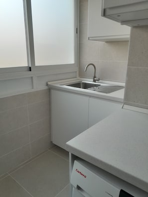 A kitchen with a stainless steel sink, white cabinets, and a Corbera dishwasher.
