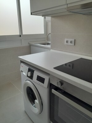 A compact kitchen with a washing machine, an oven, a sink, and a window.