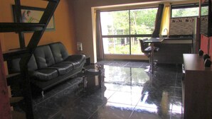 A living room with a black leather sofa, a small coffee table, and a large window with curtains. - One Bedroom Loft AC Hot Tub APT 201 (Medellin)
