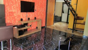 A modern interior with a flat-screen TV mounted on a red wall, a wooden entertainment unit, a brown sofa, and a staircase leading to an upper level. - One Bedroom Loft AC Hot Tub APT 201 (Medellin)