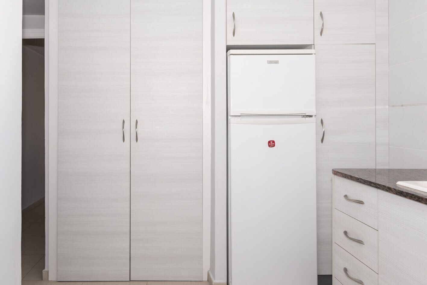 A kitchen with white cabinets, a white refrigerator, and a marble countertop.