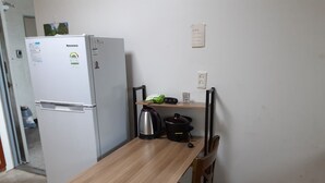 Una cocina compacta con refrigerador, una mesa de madera, un hervidor y una olla de cocción lenta.