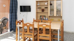 A dining area with a wooden table and chairs, a television mounted on the wall, and a cabinet with dishes. - TRIANON, 5º-29 (Cullera)