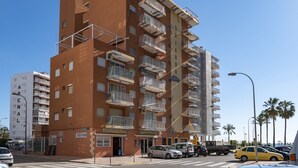 A multi-story apartment building with balconies, a storefront labeled "PANADERIA," and a street with parked cars and palm trees. - TRIANON, 5º-29 (Cullera)