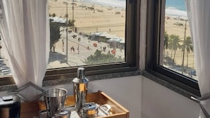 Una habitación con un amplio ventanal que da a una playa, una mesa de madera con una bandeja y un cojín estampado.