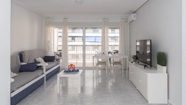 Ein modernes Wohnzimmer mit Sofa, Couchtisch, Fernseher und einem Balkon mit Blick auf Gebäude.