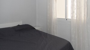Ein Schlafzimmer mit Bett, Nachttisch und einem Fenster mit durchsichtigen Vorhängen.
