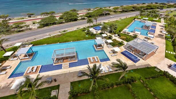A resort with a large pool, multiple sunbathing areas, and a view of the ocean. - Brand New Apartment, Panoramic Ocean Views (Noord)