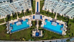 An aerial view of a modern hotel with two large swimming pools, a central courtyard, and surrounding greenery. - Brand New Apartment, Panoramic Ocean Views (Noord)